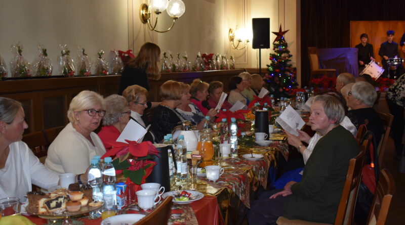 Grupa ludzi siedzi za stołem i śpiewa kolędy